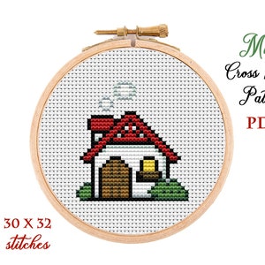 May include: A cross-stitch design of a house with a red roof, white walls, and a brown door, presented in a wooden embroidery hoop. The design includes smoke from the chimney and green bushes. Text reads "Mini Cross Stitch Pattern PDF" and "30 x 32 stitches".