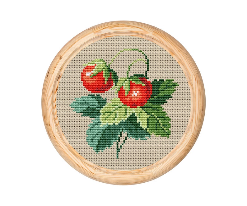 May include: A cross-stitch embroidery featuring two red strawberries with green leaves and stems, set against a beige background. The artwork is framed in a round, light-coloured wooden hoop, showcasing a handcrafted, botanical theme.