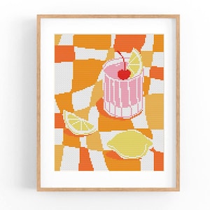 May include: Framed cross-stitch artwork depicting a pink cocktail with a cherry and lime garnish. The drink is set against a checkered orange and white backdrop, with lemon slices. The piece is presented in a wooden frame.