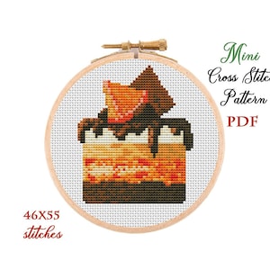 May include: A cross-stitch pattern of a slice of cake with chocolate frosting and a strawberry on top, displayed in a wooden embroidery hoop. The text "Mini Cross Stitch Pattern PDF" is visible. The pattern is 46x55 stitches.