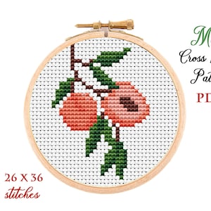 May include: A cross stitch pattern featuring two peach fruits on a branch with green leaves. The pattern is displayed on a wooden embroidery hoop and measures 26 x 36 stitches. The text "Mini Cross Stitch Pattern PDF" is displayed above the hoop.
