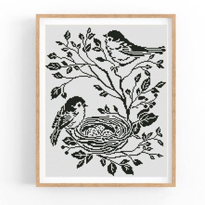May include: Black and white cross-stitch pattern of two birds on a branch with a nest and eggs. The birds are stylized and the design is simple and elegant.