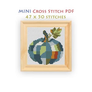 May include: A mini cross stitch PDF pattern featuring a pumpkin design with a 47 x 50 stitches count. The pumpkin is rendered in a patchwork of blue, green, orange, and white colors, framed in a light-colored wooden square frame.
