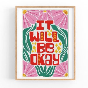 May include: A framed cross-stitch artwork with the words "IT WILL BE OKAY" in red, surrounded by green leaves and pink flowers. The artwork is in a wooden frame and is a decorative piece.