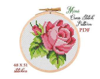 May include: A cross-stitch pattern of a pink rose with green leaves, displayed in a wooden embroidery hoop. The text "Mini Cross Stitch Pattern PDF" is visible. The pattern is 48 x 51 stitches.