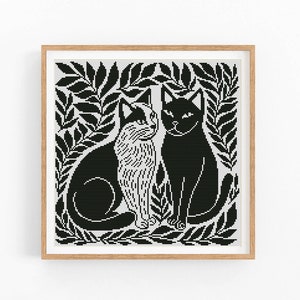 Pode incluir: Padrão de ponto cruz preto e branco de dois gatos sentados em uma moldura de folhas.