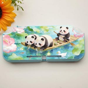 May include: A light blue Nintendo Switch case featuring a watercolor design of pandas on a bamboo raft in a pond with lily pads and a duck. The case has a floral and water theme.
