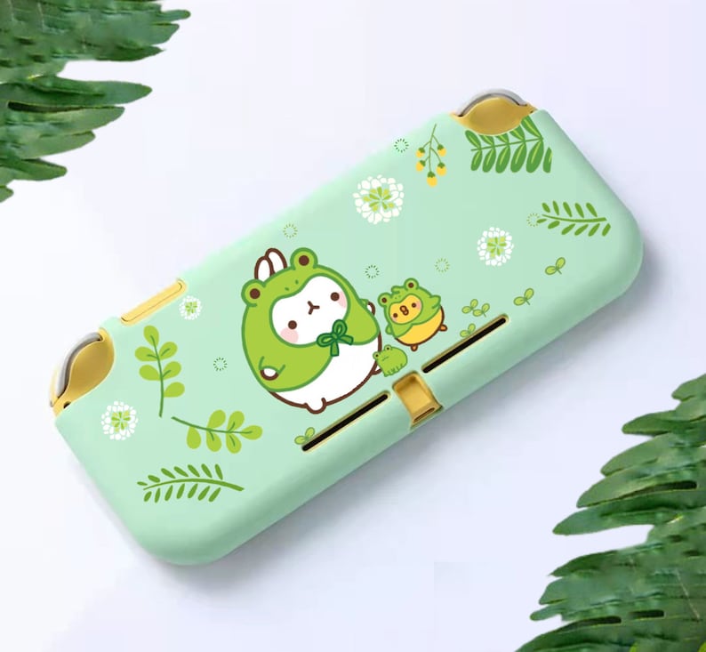 Puede incluir: Una funda verde claro para Nintendo Switch Lite con un dise&ntilde;o de rana de dibujos animados. La funda tiene un acabado mate e incluye un personaje de rana grande con un sombrero de rana, con dos personajes de rana m&aacute;s peque&ntilde;os. El dise&ntilde;o se complementa con detalles florales y de hojas.