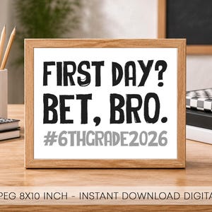 May include: A rectangular wooden frame containing a white sign with black text that reads FIRST DAY? BET, BRO. and grey text that reads #6THGRADE2026. The sign is displayed on a wooden surface with notebooks and a pencil holder nearby.