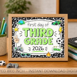 May include: A framed sign with a black and white speckled background featuring the text first day of THIRD GRADE 2026 in green and black. The design includes illustrations of a cap, race car, star, peace sign, soccer ball, game controller, sunglasses, fire, and a speech bubble with the word BRUH.
