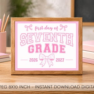 May include: A framed sign with a white background and pink border featuring the text "first day of SEVENTH GRADE" in pink varsity-style lettering. The design includes pink bow illustrations and the years "2026" and "2027" in pink text.