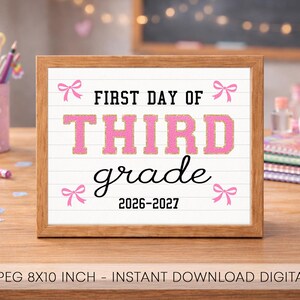 May include: A rectangular wooden frame containing a white sign with horizontal lines. The text reads FIRST DAY OF THIRD grade 2026-2027 in black and pink glittery letters. Four small pink bows are positioned in the corners of the sign.