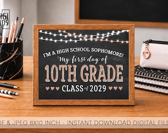 May include: A rectangular wooden frame containing a black chalkboard-style sign with white string lights at the top. The text reads: I'M A HIGH SCHOOL SOPHOMORE! My first day of 10TH GRADE CLASS of 2029. The sign features rose gold glitter lettering.