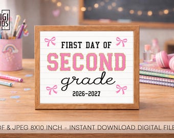 May include: A rectangular wooden frame containing a white sign with horizontal lines. The text reads FIRST DAY OF SECOND grade 2026-2027 in black and pink varsity-style lettering. Four small pink bows are positioned in the corners of the sign.