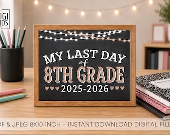 May include: A framed chalkboard sign with the text "MY LAST DAY of 8TH GRADE 2025-2026" in white and rose gold lettering. The sign is on a wooden desk with pencils, pens, and notebooks.