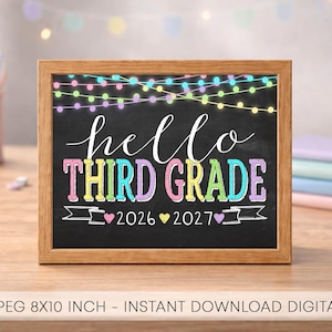 Pode incluir: Uma moldura de madeira retangular contendo uma lousa preta com o texto hello THIRD GRADE 2026 2027. O design apresenta luzes coloridas no topo e pequenos corações entre os anos. A placa mede 20x25 cm.