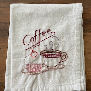 May include: White kitchen towel with embroidered coffee cup and cupcake with the word "Coffee" in red cursive.