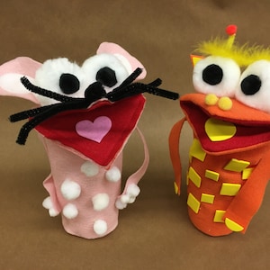 May include: Two felt hand puppets, one pink with white polka dots and a red heart, the other orange with yellow squares and a yellow heart.