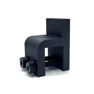 May include: Black plastic clamp with two adjustable screws. The clamp has a rectangular shape with a rounded opening on one side.