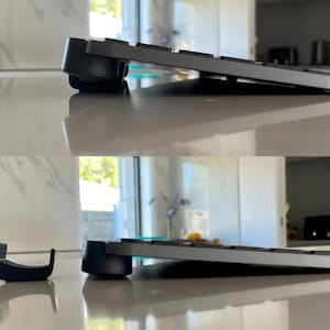 Puede incluir: Dos imágenes de un teclado negro con un soporte negro. El teclado está inclinado hacia arriba y el soporte está en la esquina inferior derecha de la imagen. El soporte es una pequeña pieza de plástico negro diseñada para sostener el teclado.