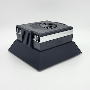 Può includere: Dispositivo elettronico nero con una ventola sulla parte superiore, dettagli argentati e la scritta "PopBloom" sul lato. Il dispositivo poggia su una base nera angolata. La ventola ha più pale.