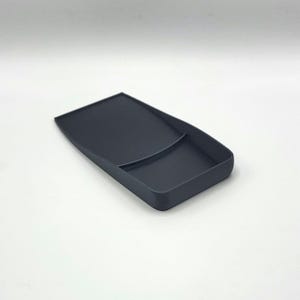 Puede incluir: Una bandeja de pl&aacute;stico gris oscuro con una secci&oacute;n dividida. La bandeja est&aacute; dise&ntilde;ada para contener objetos peque&ntilde;os, como joyas o monedas.
