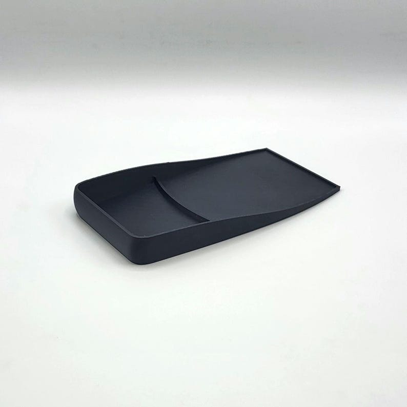 Puede incluir: Una bandeja de pl&aacute;stico negro con un borde curvo y una peque&ntilde;a hendidura rectangular. La bandeja est&aacute; dise&ntilde;ada para contener objetos peque&ntilde;os, como joyas o monedas.