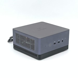 May include: A dark gray mini-computer with the brand name "MINISFORUM" on the top. The device has a power button, USB ports, and a ventilation grill. The base is black, and the overall design is compact and modern.