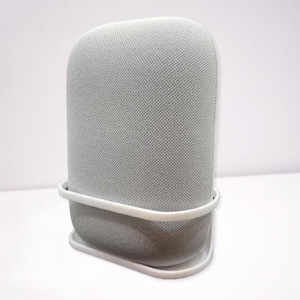 Puede incluir: Un altavoz blanco cubierto de tela con una base de plástico blanco. El altavoz tiene una forma redondeada y una superficie texturizada.