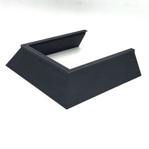 Puede incluir: Un soporte de plástico negro con una abertura cuadrada en el centro. El soporte tiene una base elevada y está diseñado para elevar un objeto.