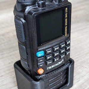 May include: Black multi-band amateur transceiver with a screen and multiple buttons, including 'BT' and 'V/M'. The radio is in a black holder. The text 'TIDRADIO' is visible.