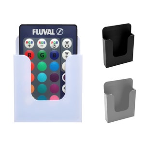 May include: White plastic remote control holder with a blue remote control inside. The remote control has a black face with white buttons and the text "Fluval" on it. There is also a black and a gray holder in the image.