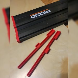 May include: Two red plastic pieces with a black and orange RIDGID logo on a wooden surface. The pieces are used to extend the length of a tool.