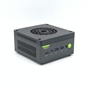 May include: A dark gray mini computer with a fan on top and multiple ports on the front. The front of the device has USB and other ports, along with a power button. The device has a green sticker on the side.