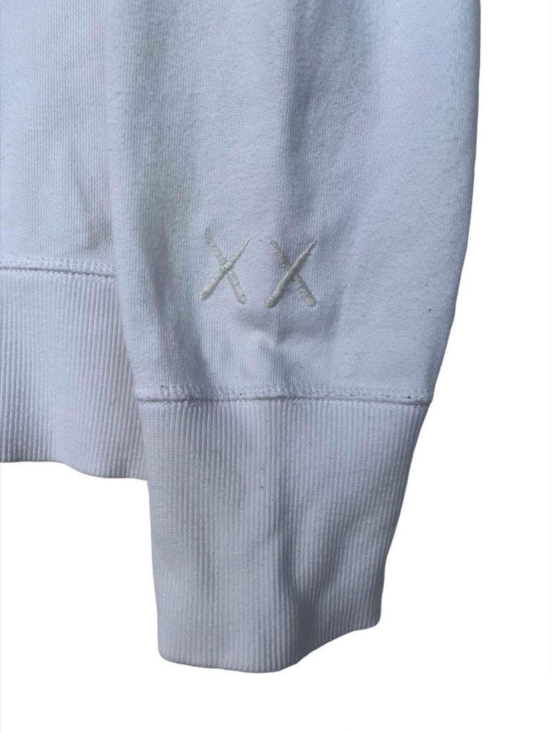 以下が含まれることがあります： 左袖にリブの袖口と小さな刺繍の「XX」ロゴが付いた白い長袖スウェットシャツです。