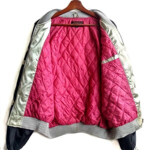 May include: A black and silver satin bomber jacket with a pink quilted lining. The jacket has a grey ribbed collar, cuffs, and waistband.