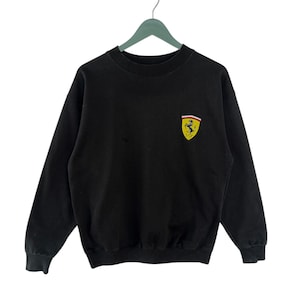 May include: Black sweatshirt with a yellow and red Ferrari logo on the front.