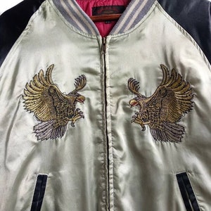 May include: A light green satin bomber jacket with black sleeves and a zipper closure. The jacket features embroidered golden eagles on the front and a red and gray striped collar.