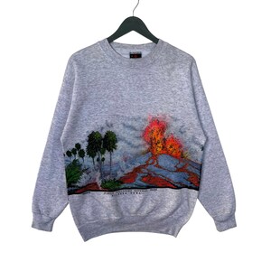 May include: Gray sweatshirt with a colorful graphic print of a volcano erupting in Hawaii Volcanoes National Park. The text "Hawaii Volcanoes National Park, Big Island, Hawaii" is printed below the graphic.