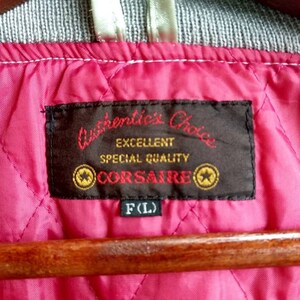 May include: A black label with white text that reads "Authentic's Choice Excellent Special Quality CORSAIRE" with two gold stars on either side of the text. The label is attached to a pink quilted fabric with a white tag that reads "F(L)".