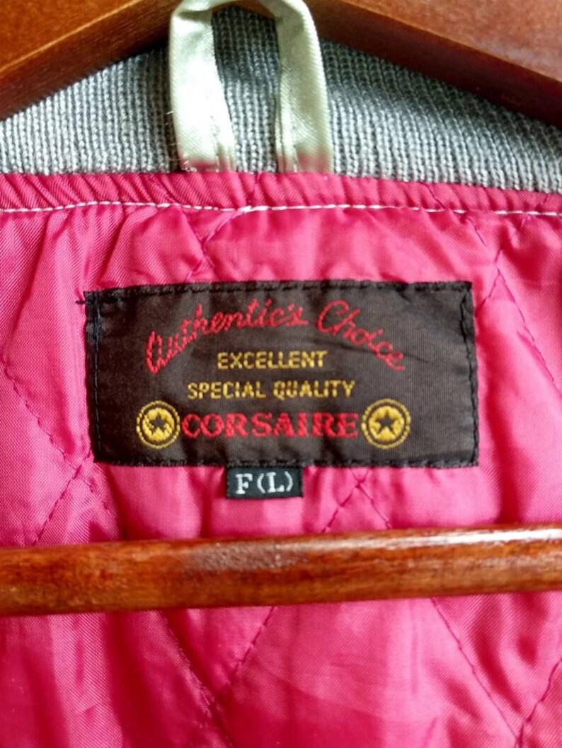 May include: A black label with white text that reads "Authentic's Choice Excellent Special Quality CORSAIRE" with two gold stars on either side of the text. The label is attached to a pink quilted fabric with a white tag that reads "F(L)".