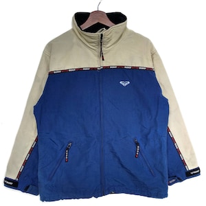 May include: A blue and beige fleece jacket with a zip closure and a logo on the front. The jacket has a high collar and a black fleece lining. The jacket has a "ROXY" logo on the zip pull and on the side of the jacket.