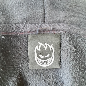 May include: Black hoodie with a black label featuring a white flame logo with a grinning face.