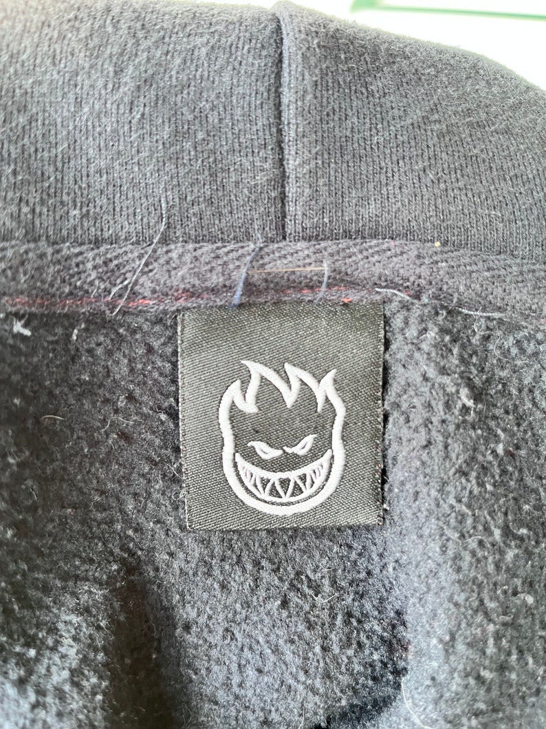 May include: Black hoodie with a black label featuring a white flame logo with a grinning face.
