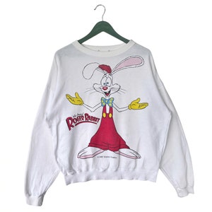 May include: White long-sleeve sweatshirt with a cartoon image of Roger Rabbit from the movie "Who Framed Roger Rabbit?" The image shows Roger Rabbit in his signature red overalls and yellow gloves. The text "Who Framed Roger Rabbit?" is printed below the image. The sweatshirt has a crew neck and long sleeves.