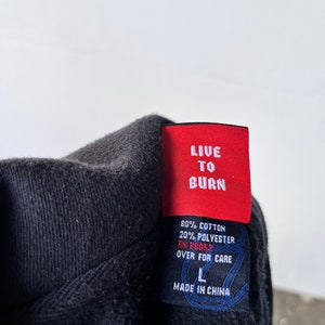 May include: A black hoodie with a red tag that says "LIVE TO BURN". The tag also includes the fabric content, RN number, and care instructions. The hoodie is size L and made in China.