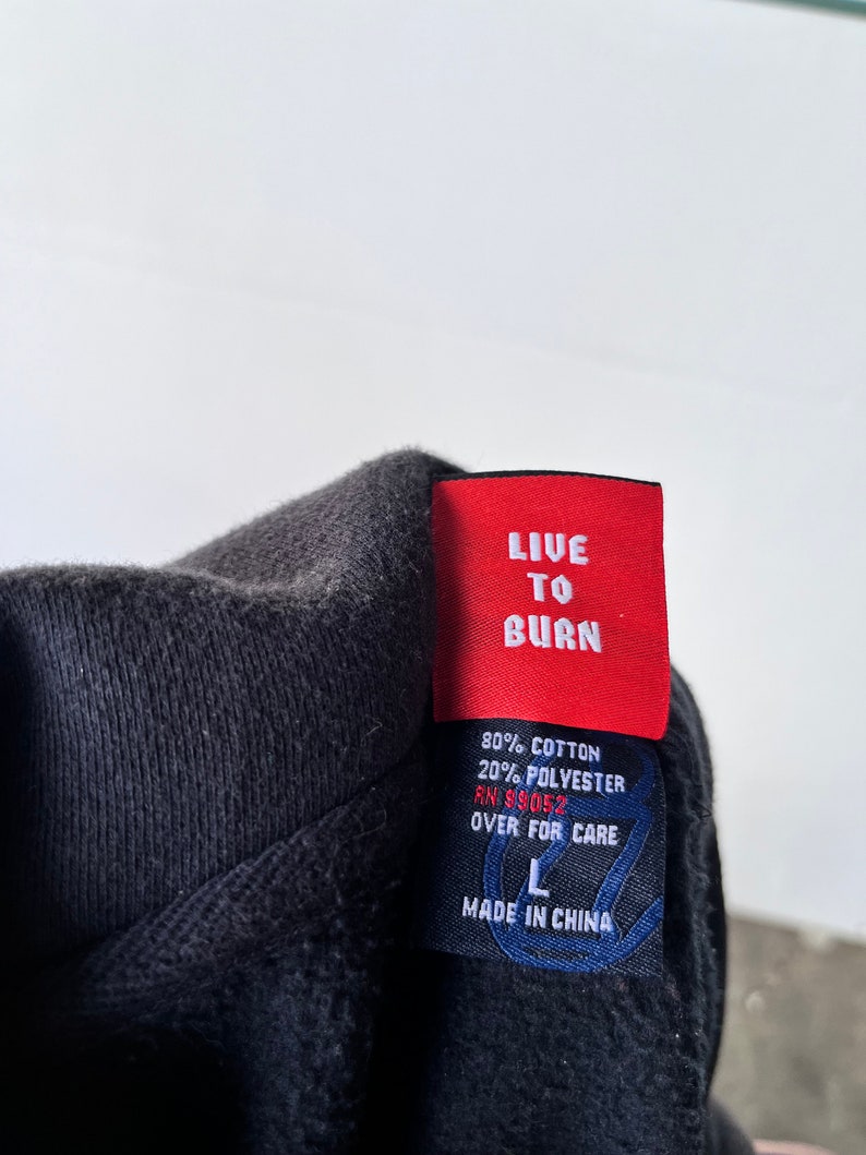 May include: A black hoodie with a red tag that says "LIVE TO BURN". The tag also includes the fabric content, RN number, and care instructions. The hoodie is size L and made in China.