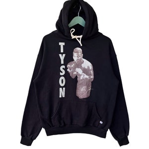 May include: Black hooded sweatshirt with a white graphic of Mike Tyson boxing. The graphic includes the text "TYSON" and Mike Tyson's signature.