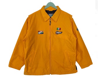 May include: A yellow zip-up jacket with black accents and multiple patches. The patches feature a car, a flag, and a logo with the text "Formula 1".