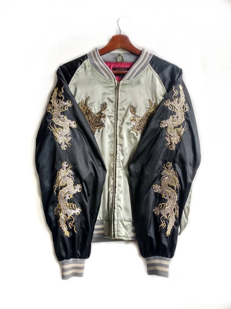 May include: A black and light green satin bomber jacket with gold embroidered dragons on the sleeves and eagles on the front. The jacket has a zipper closure and ribbed cuffs and collar.